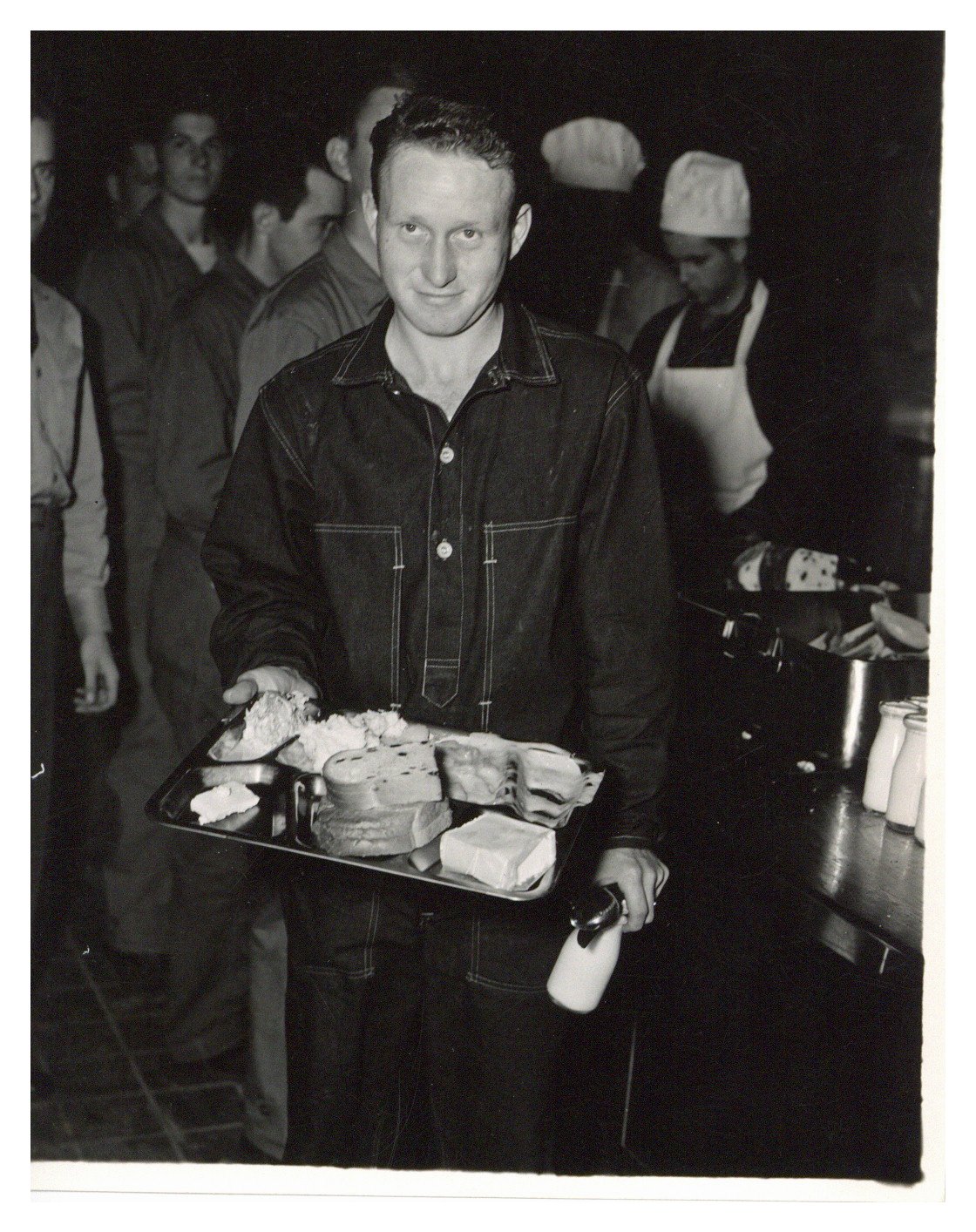 A man holding a cafeteria tray in one hand and a bottle of milk and silverware in one of Chanute's dining halls. 