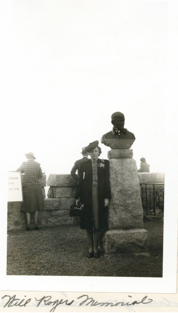 Black and white photograph of Mary Ellen standing next to a bust of Will Rodgers in Colorado Springs, CO.
