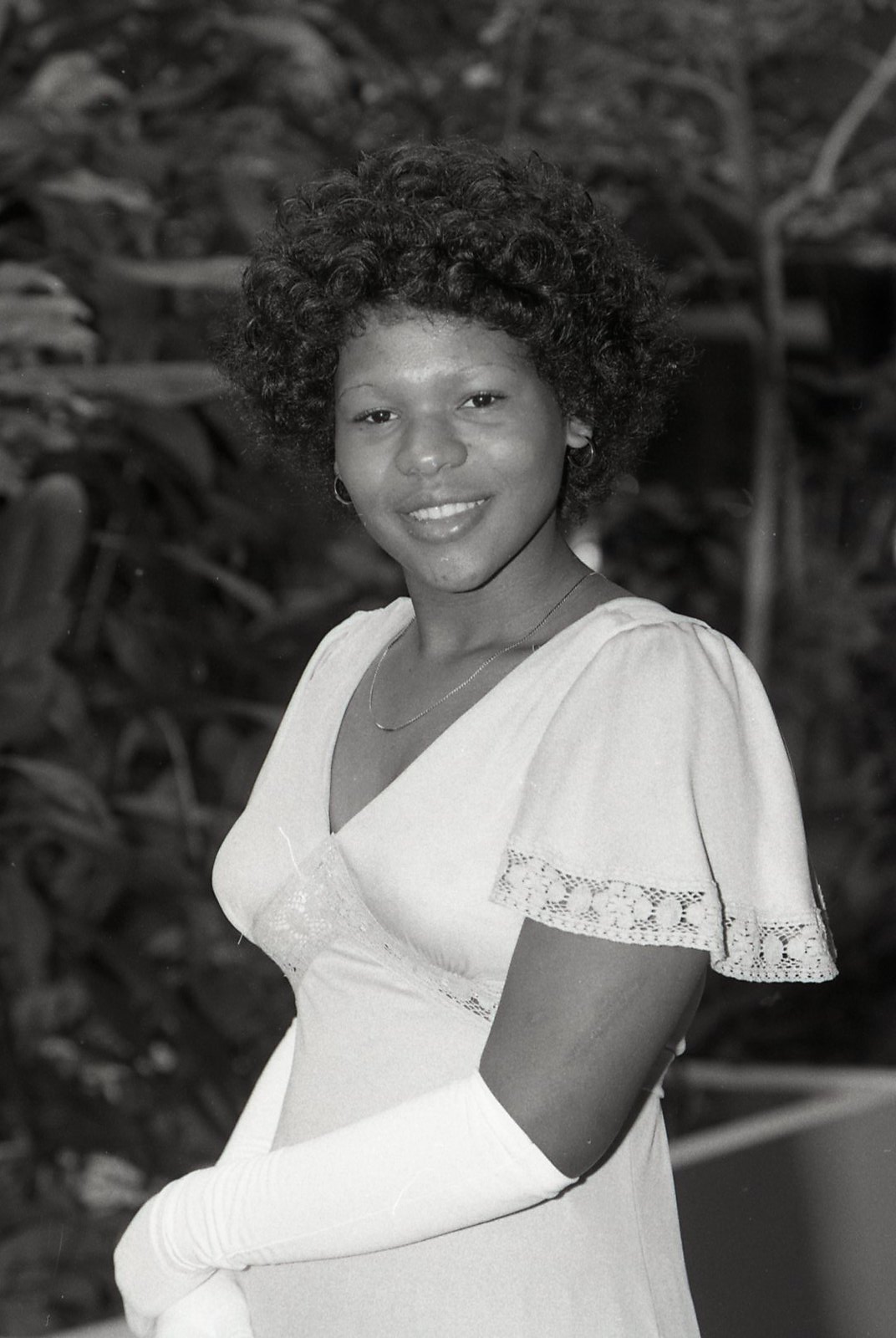 Black-and-white photograph of a young African American woman wearing a white dress and gloves, smiling at the camera.