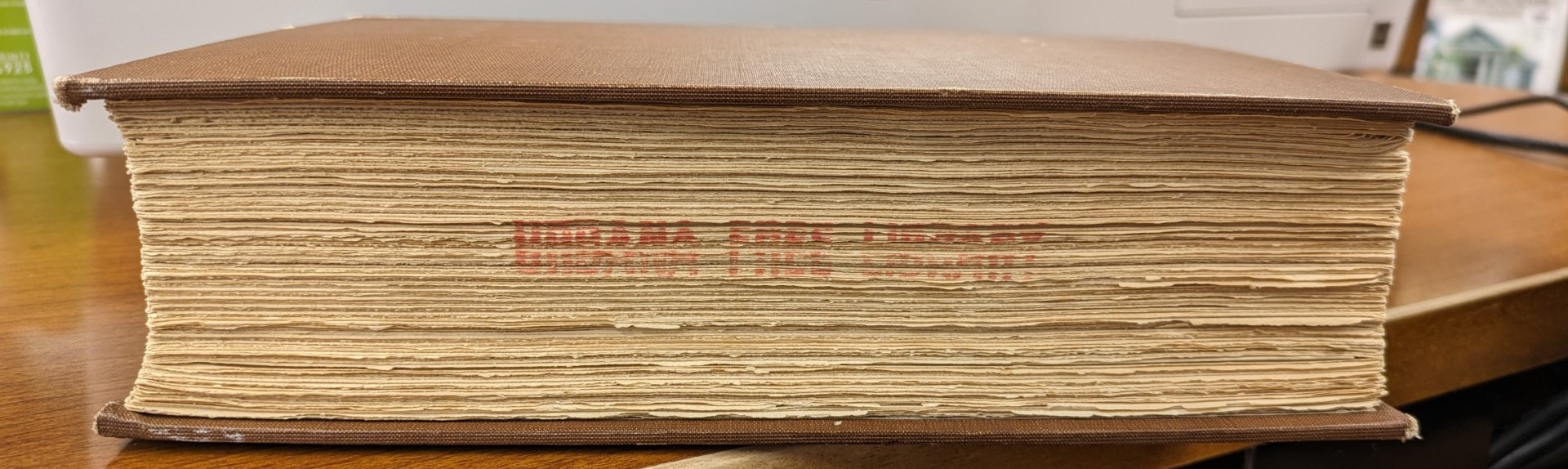 A color photograph of the fore edge of a brown leather bound book. Urbana Free Library is stamped in red on the paper.