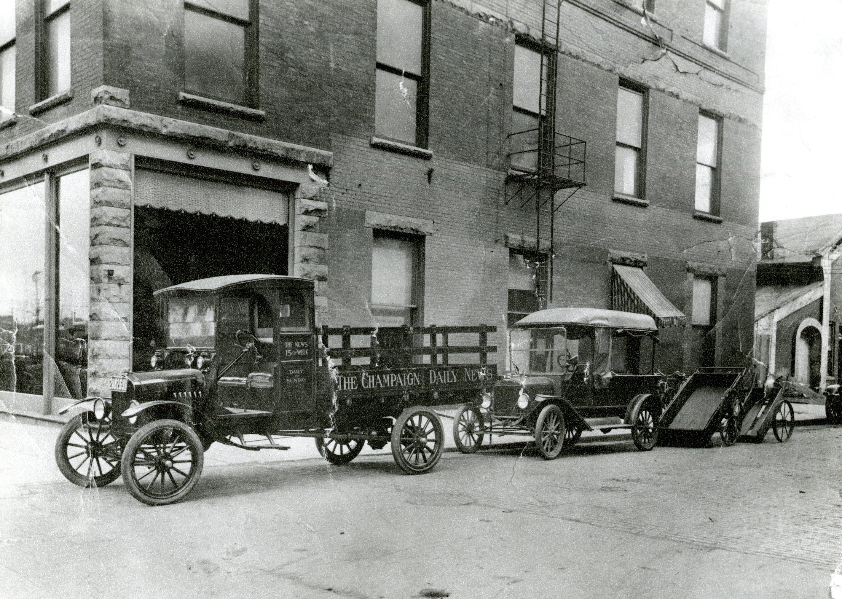 Photograph of the Champaign Daily News (future News-Gazette) office with delivery trucks parked outside.