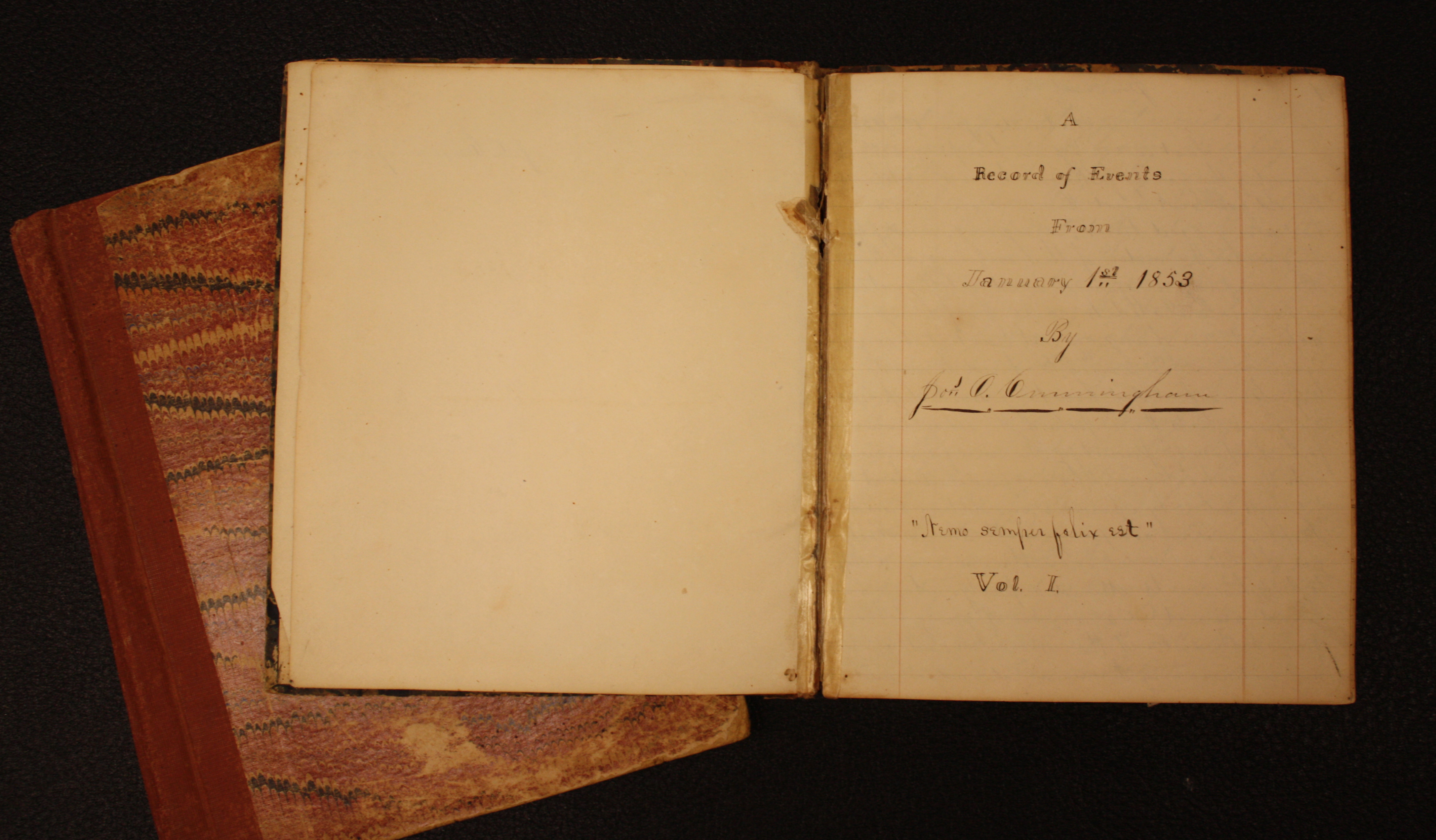 A top-down view of an open journal laying on a table. The text on the page reads, "A Record of Events from January 1st 1853 by Jos. O. Cunningham "Aemo Semper Felix Est" Vol. I."