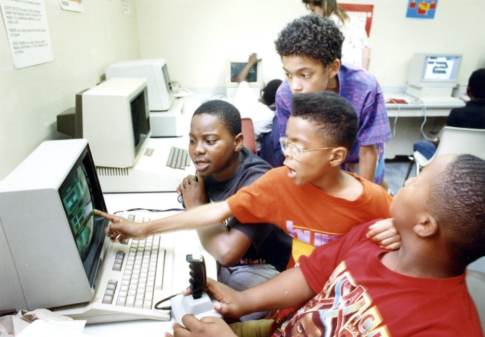 A color photograph of four young Black students using a computer together.