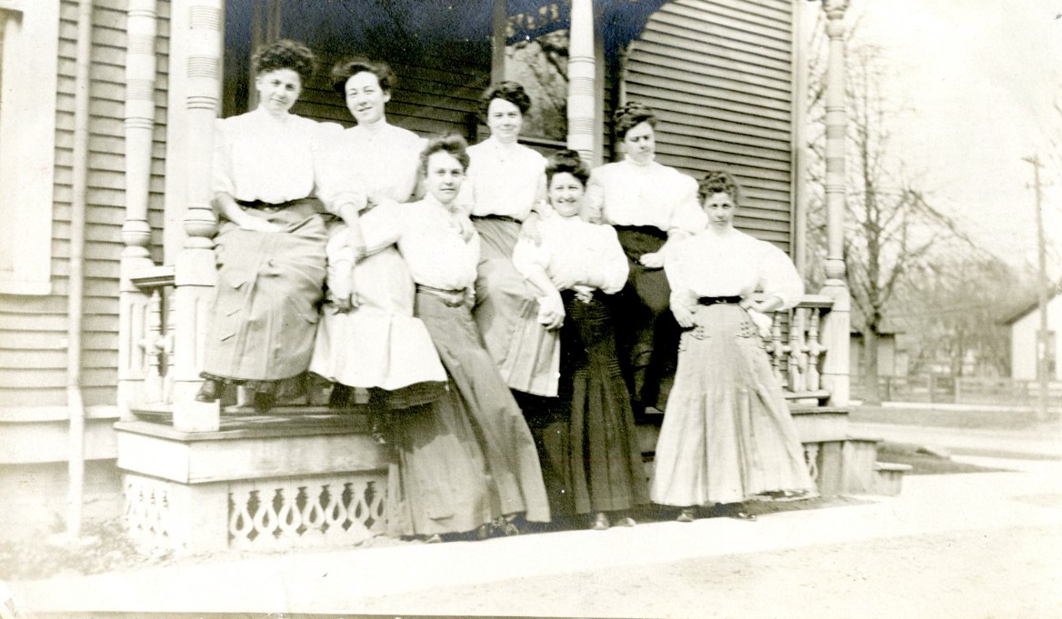 A black and white photograph of a group of women posing outside of a house.