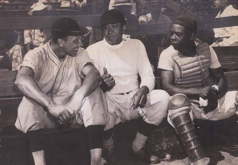 A black and white photograph of three baseball players talking and sitting in the dugout. From left to right: Ray Thomas, Eddie Glover, and Rubavent Utley, from the Urbana Courier on July 12, 1942.