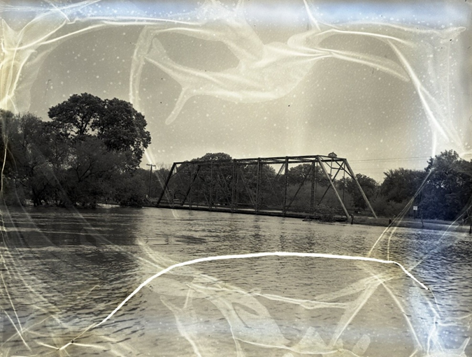 Black and white negative of a flood in Fisher, Illinois. A bridge is visible above a flooded river. The negative is warped due to vinegar syndrome.