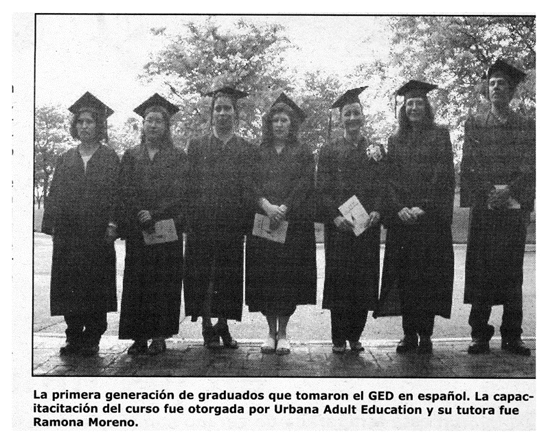 A black and white photograph printed in the paper of Urbana's first graduating class of Spanish speaker GED recipients. Seven people in caps and gowns smile at the camera.