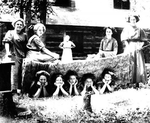 Group of women posing near and under a blanket on a clothes line. 